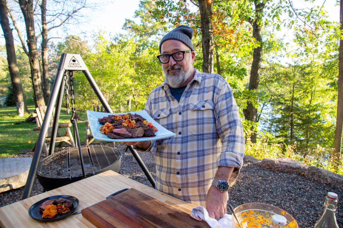 A man holds a plate of cooked venison outside