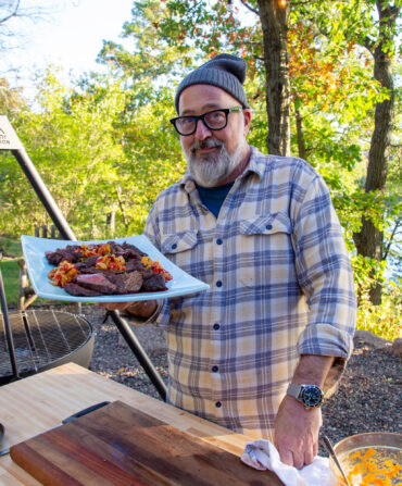 A man holds a plate of cooked venison outside