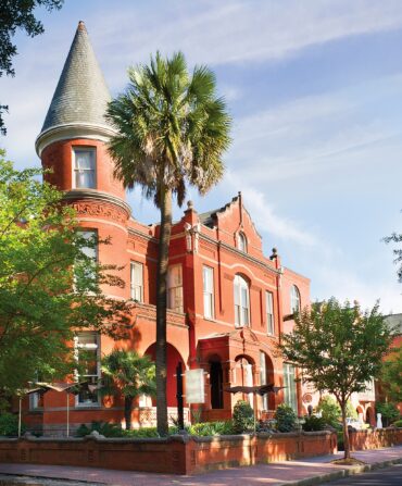 A stately brick building in a tree-covered street