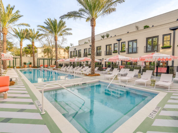 A hotel pool piazza with pink umbrellas, lounge chairs, and striped floor detailing