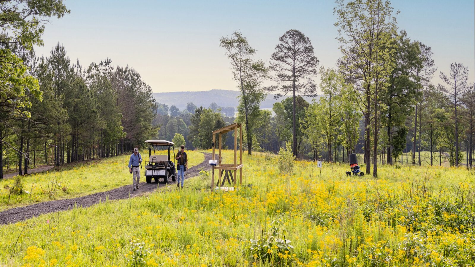 Two men approach a shooting station in a field spotted with trees