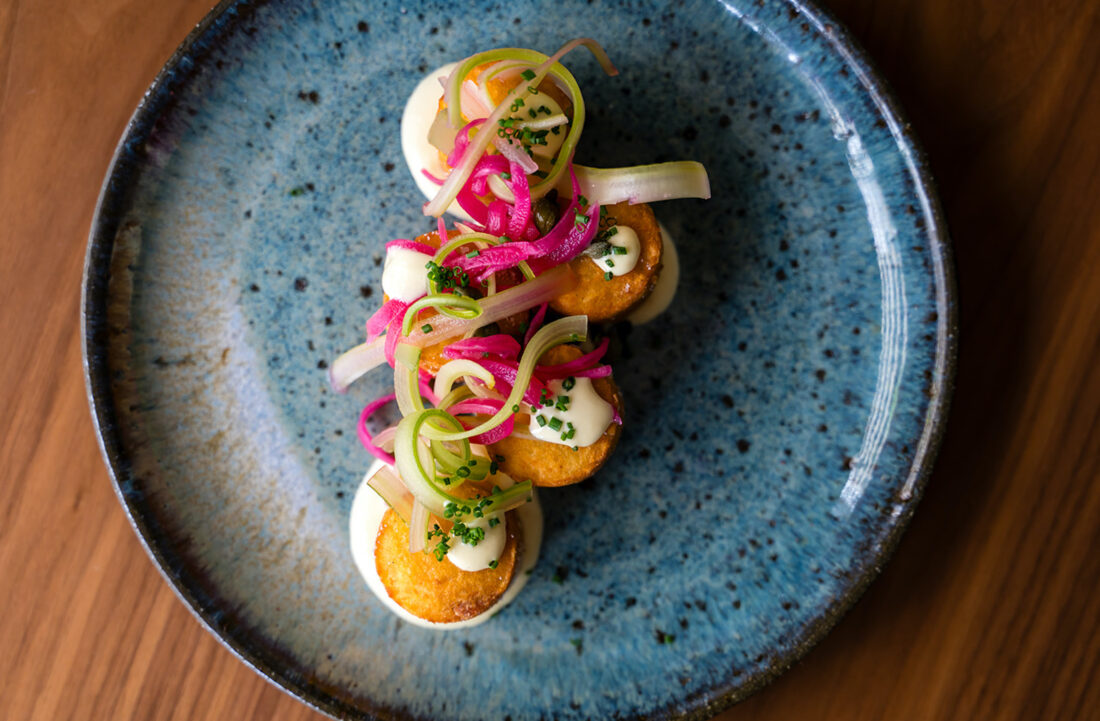 A dish of tater tots topped with pickled red onion