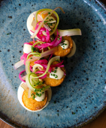 A dish of tater tots topped with pickled red onion