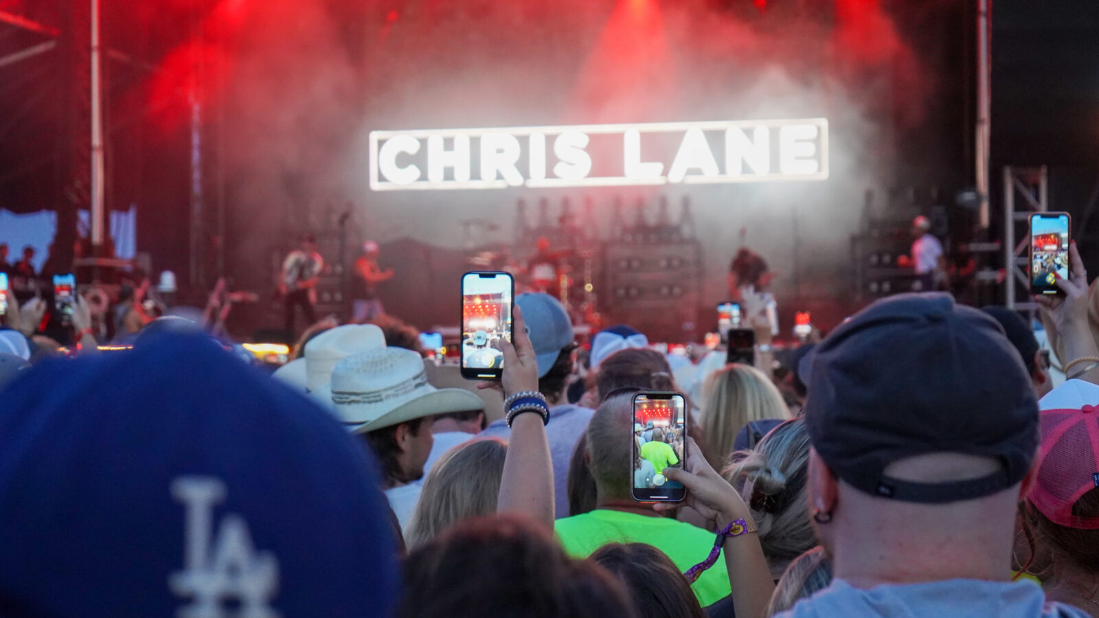 A crowd in front of a stage at a festival; people hold up phones to record the show