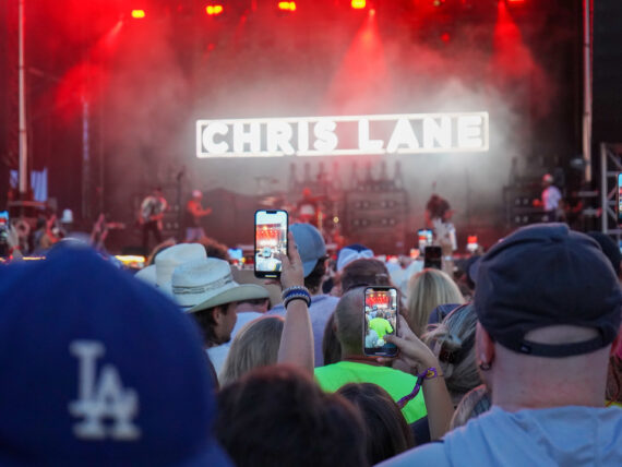 A crowd in front of a stage at a festival; people hold up phones to record the show
