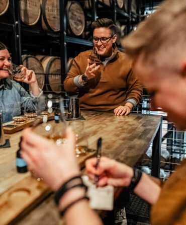 People at a table laugh and drink bourbon and take notes