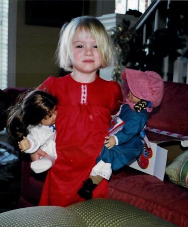 A little girl holds two american girl dolls