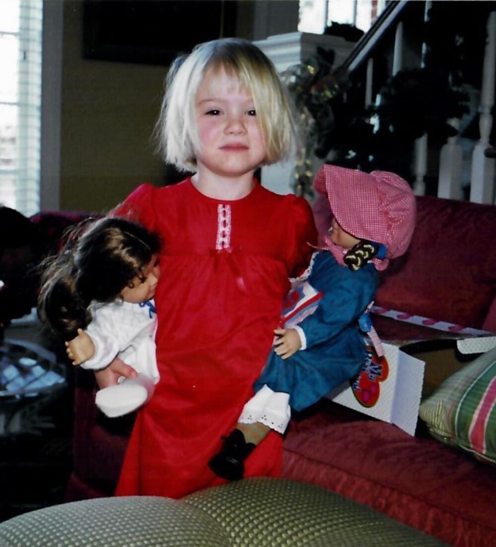A little girl holds two american girl dolls