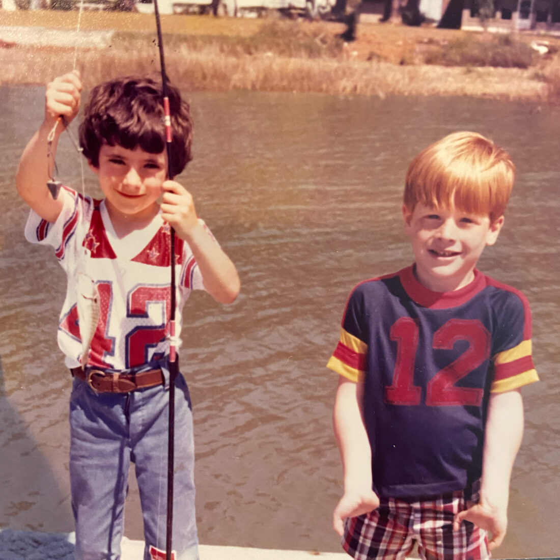Two boys, one holding a fish on a pole