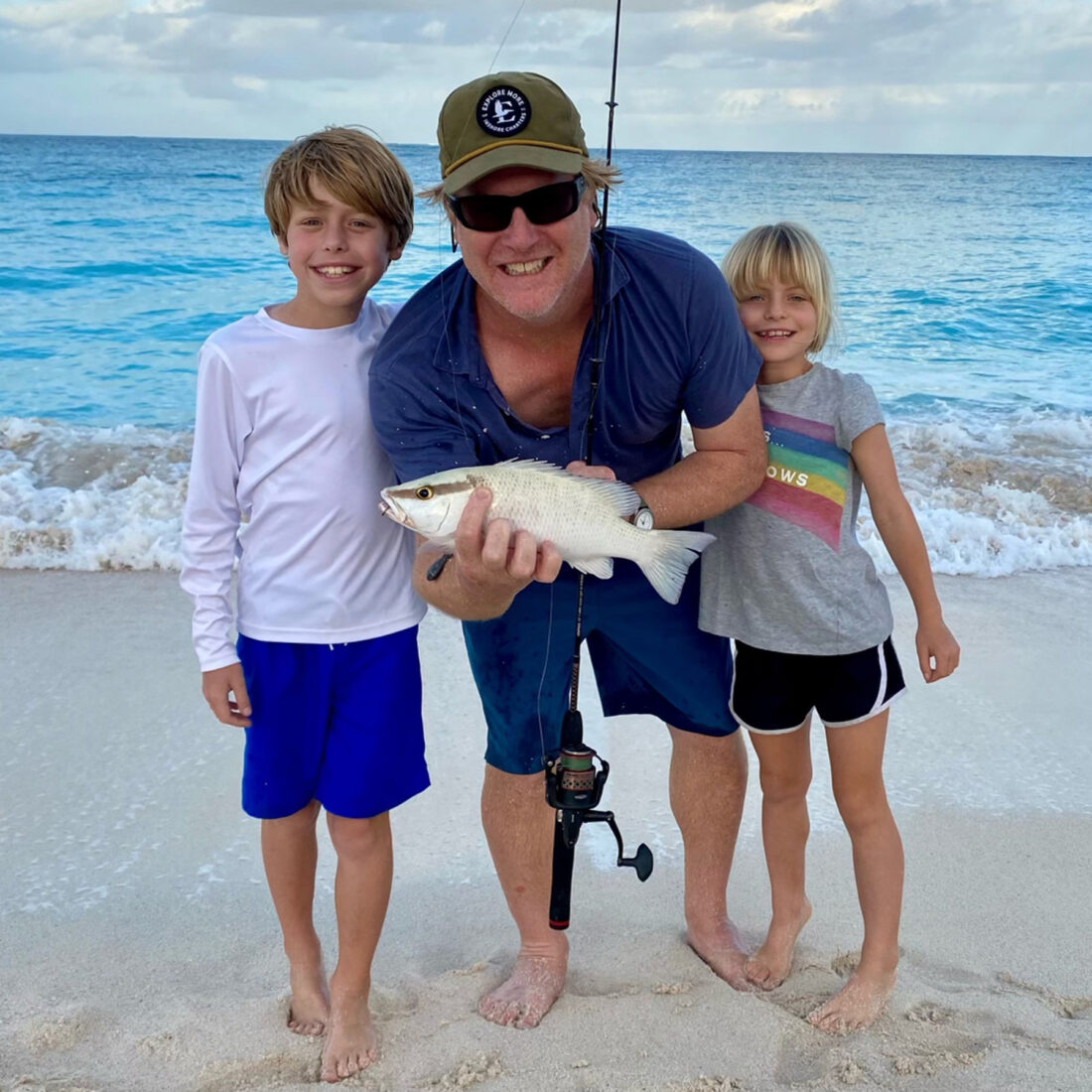 A man holds a fish while his two kids stand on either side of him