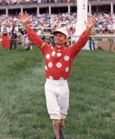 A jockey in a red and white silk raises his arms to the sky