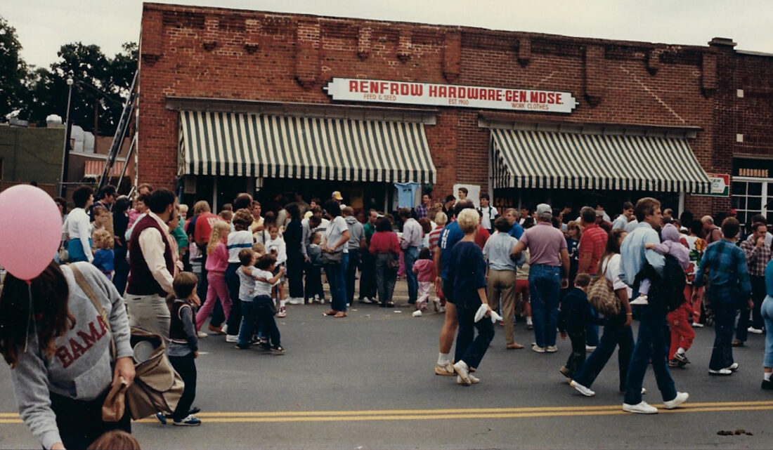 A vintage photo of a hardware storefront with a crowd of people in front of it