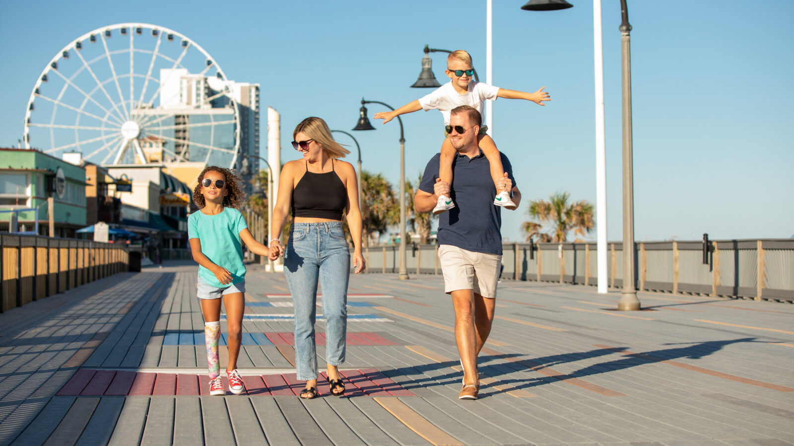 A family walks down a boardwalk with a ferris wheel