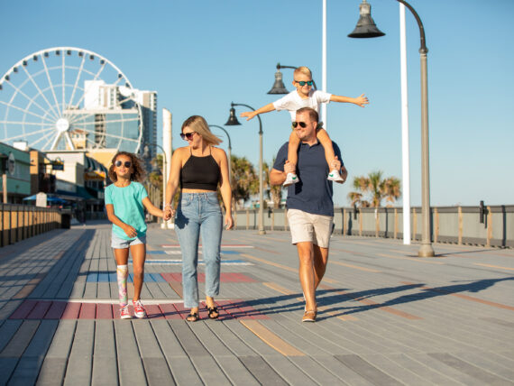 A family walks down a boardwalk with a ferris wheel