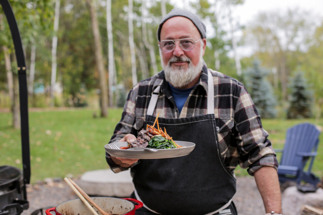 A man holds a dish with red wine braised duck with spinach and potato strings