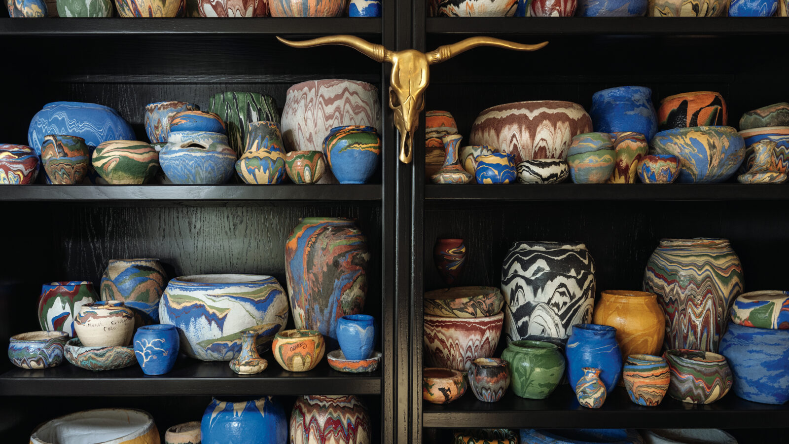 Mathis’s 150-vessel-strong Ozark Roadside Tourist Pottery collection in his Oklahoma City living room. The vessels have swirling, colorful patterns.