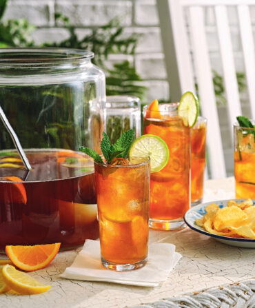 Sweet tea punch in a glass with a larger pitcher and sliced oranges