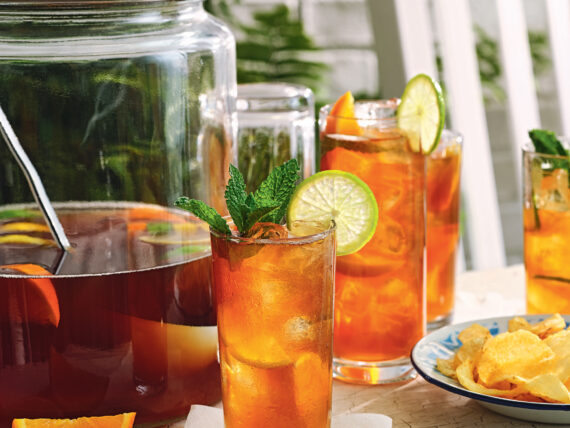 Sweet tea punch in a glass with a larger pitcher and sliced oranges
