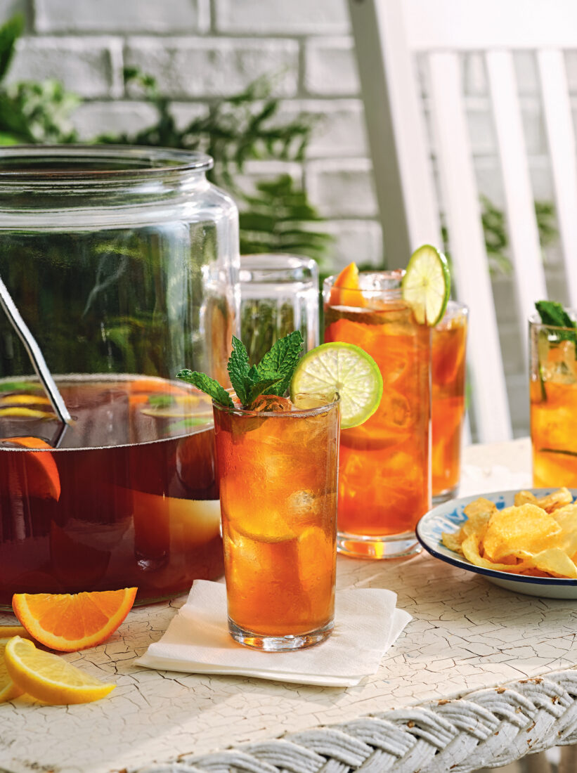 Sweet tea punch in a glass with a larger pitcher and sliced oranges