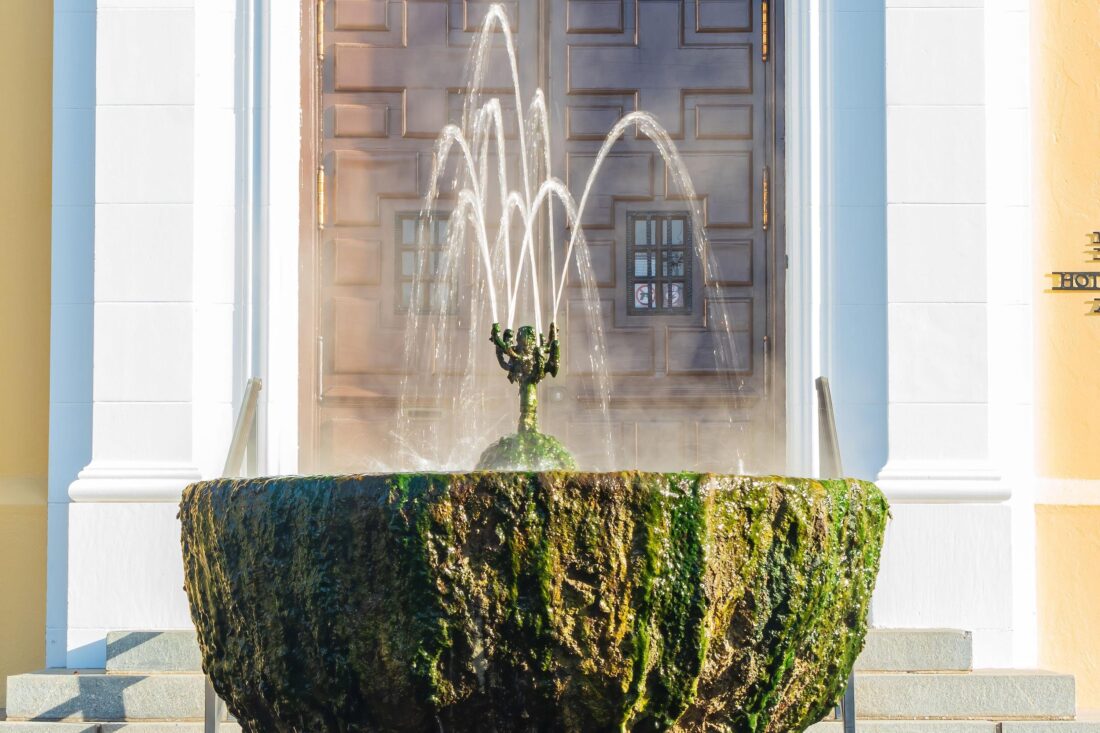 A fountain spills water over a mossy fountain bowl