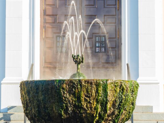 A fountain spills water over a mossy fountain bowl