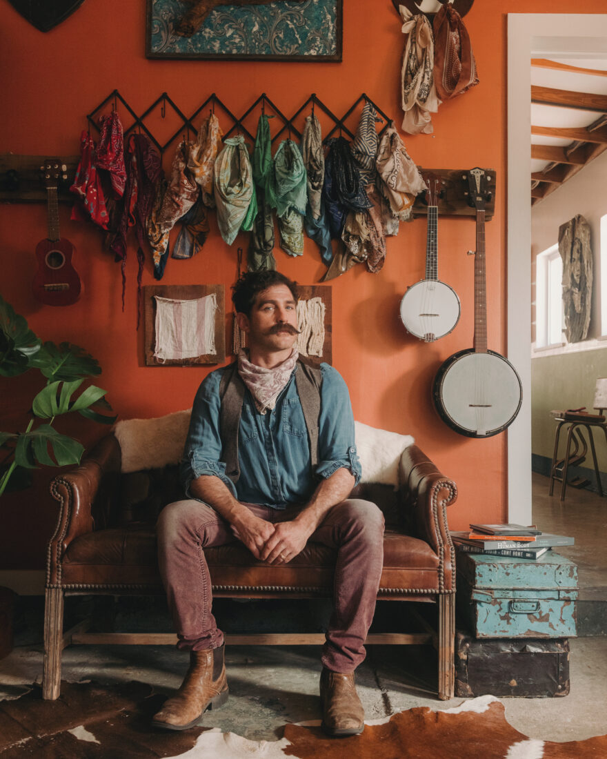 A portrait of a man with a curly mustache, sitting in an orange room
