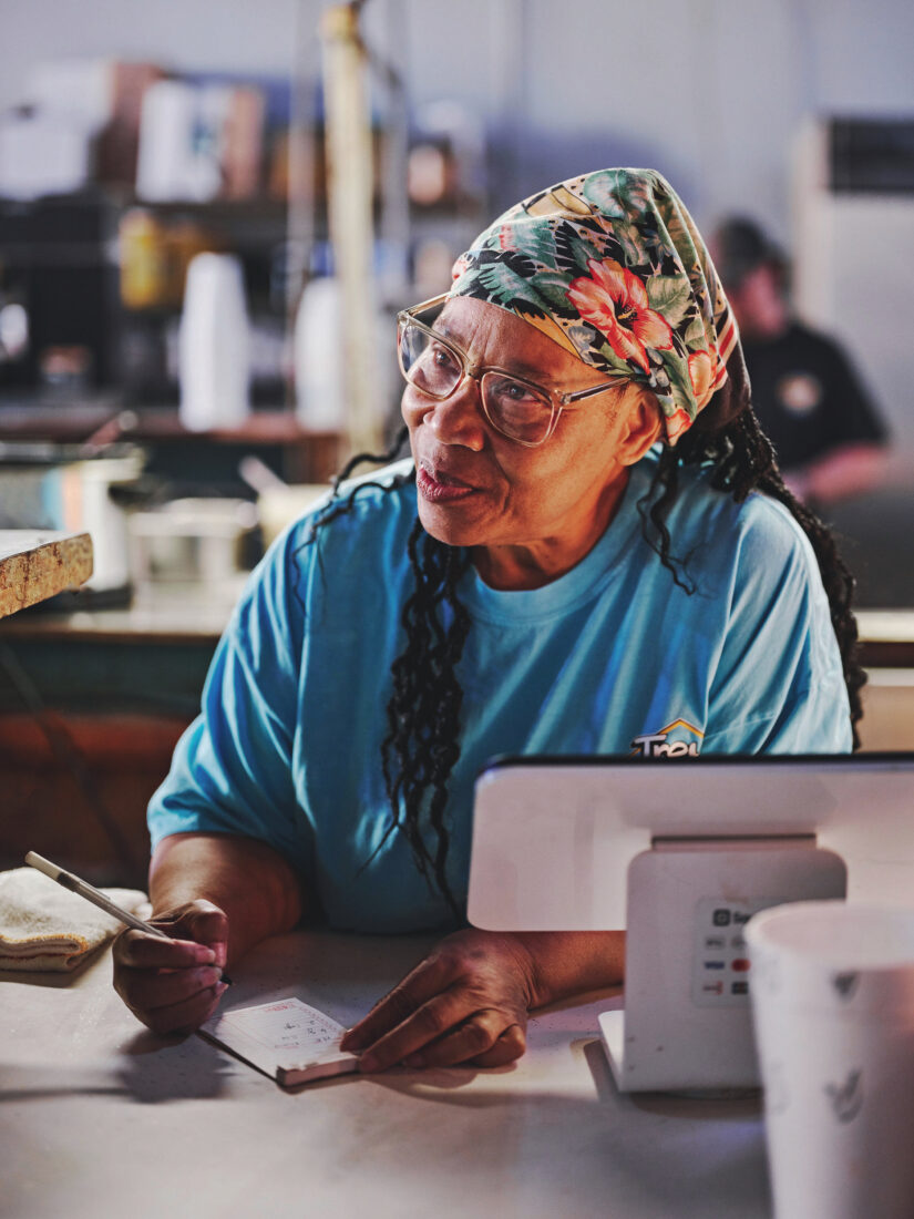 A woman stands behind a counter with a pad and pencil