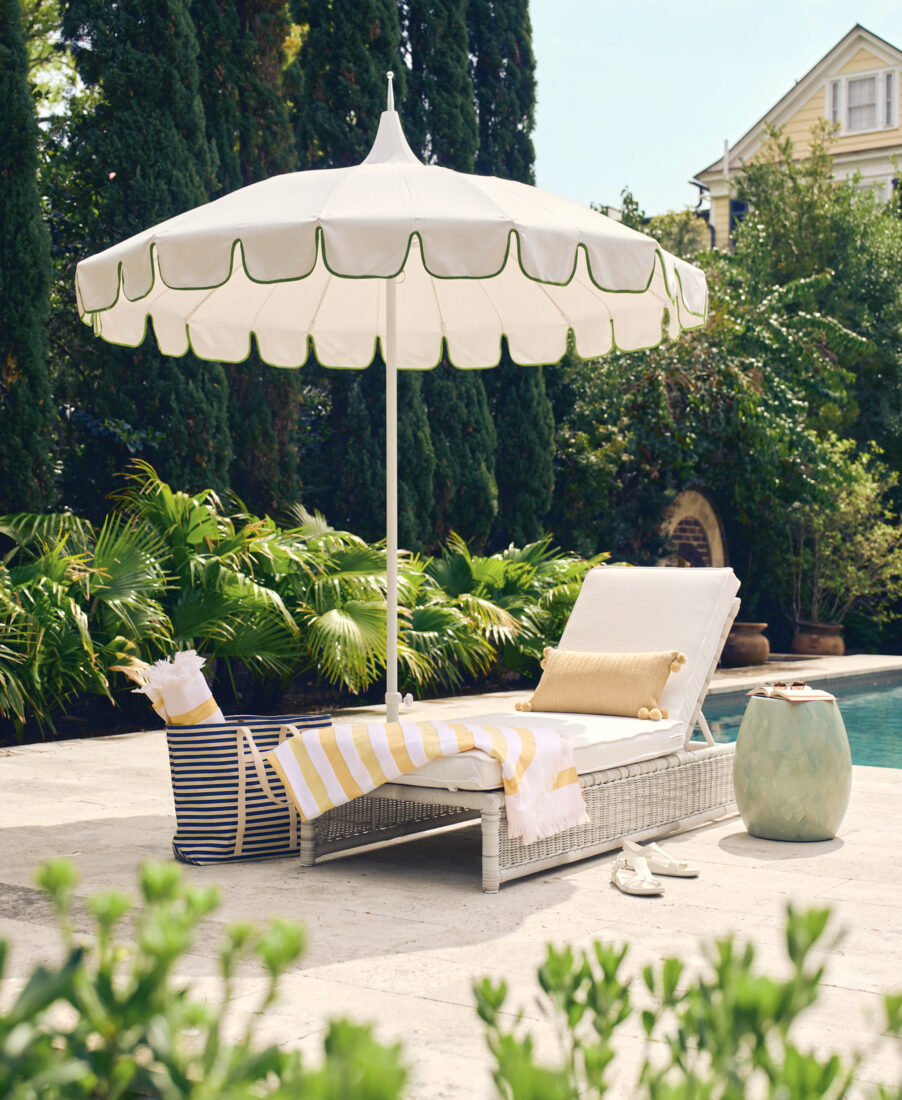 A poolside scene with a white and green umbrella, lounger, and tote bag