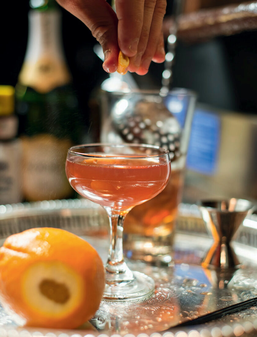 A hand adds an orange twist to a drink