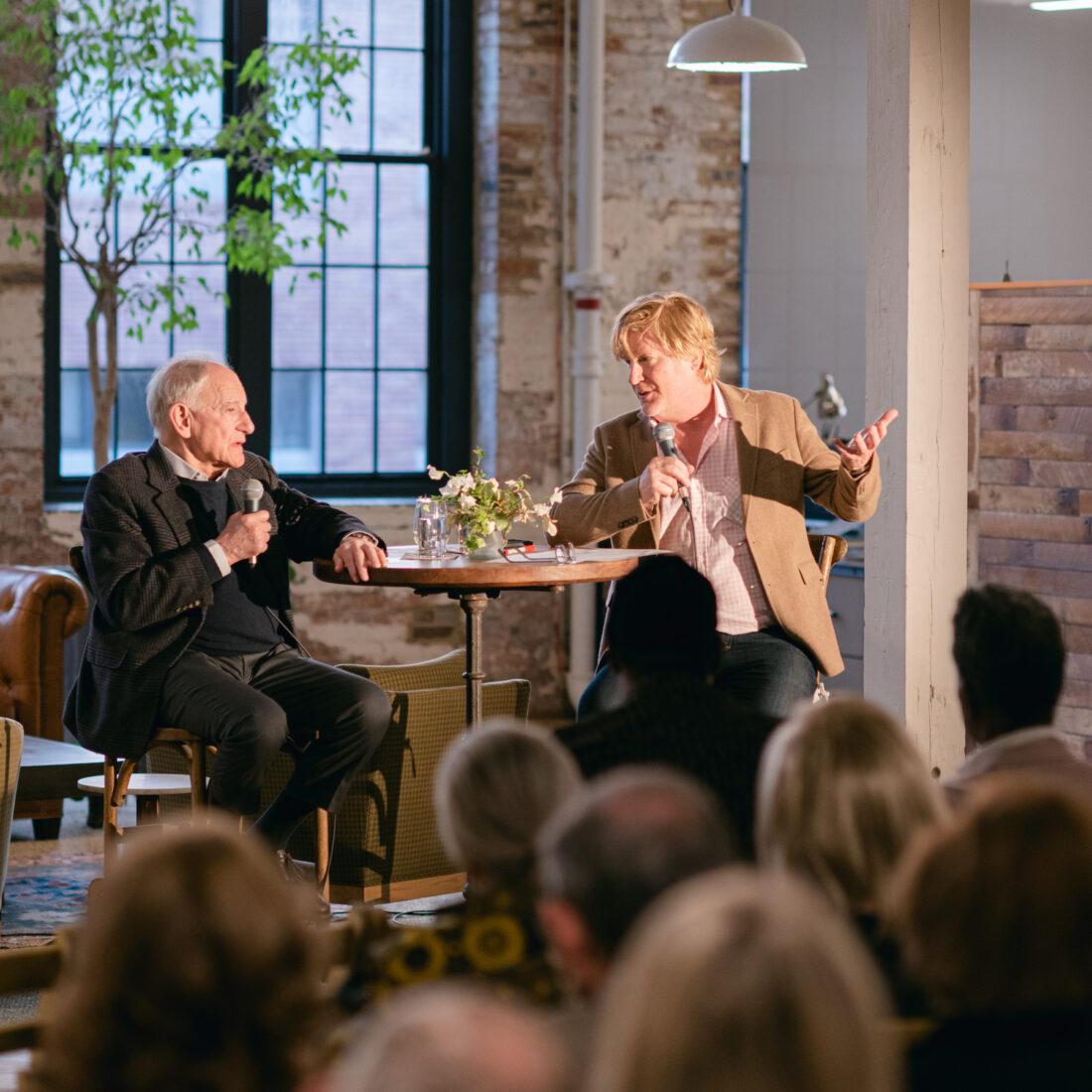 Two men sit at a table during an interview in a rustic office.