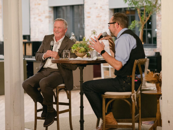 John Grisham and Jonathan Miles hold microphones while sitting next to each other at a table