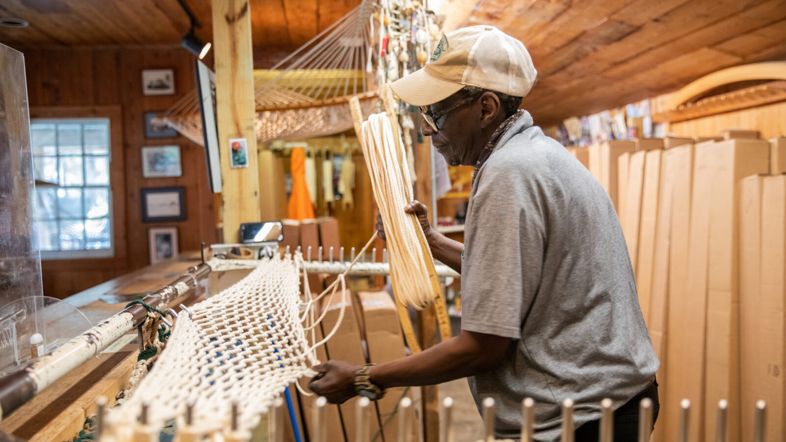 A man weaves a hammock on a stand in a shop