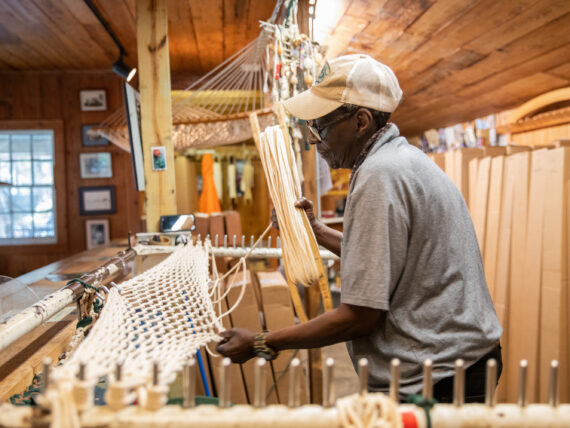 A man weaves a hammock on a stand in a shop