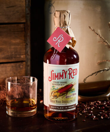 A bottle of bourbon with a partly filled glass on a table