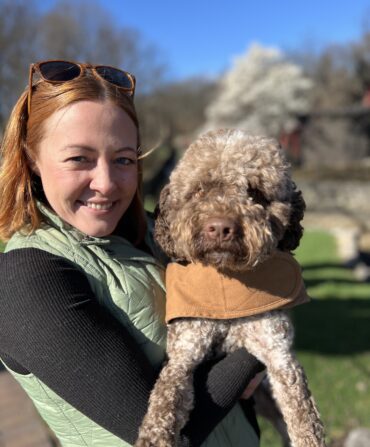 A woman holds a brown poodle dog