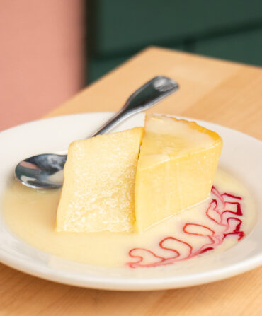 A plate with a slice of yellow bread pudding with a drizzle of raspberry