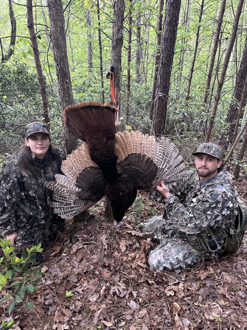 Two hunters kneel with a turkey with blonde-tinged feathers