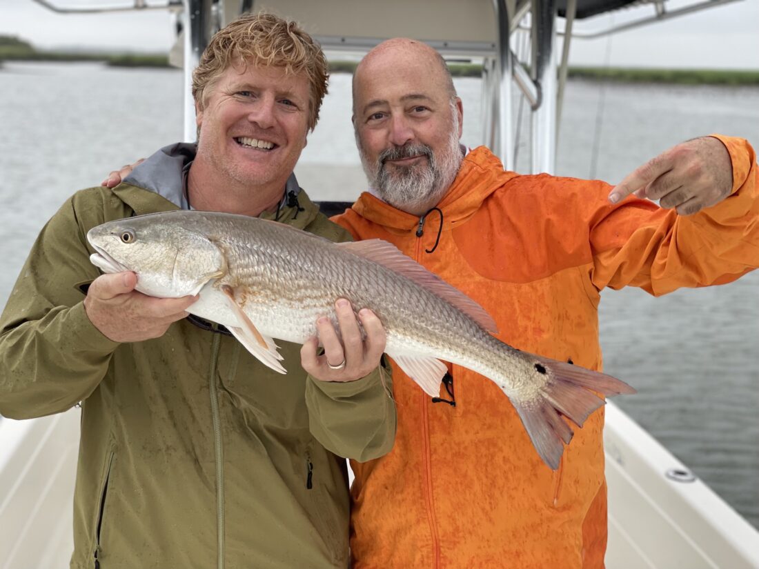 Two men pose with a redfish on a boat