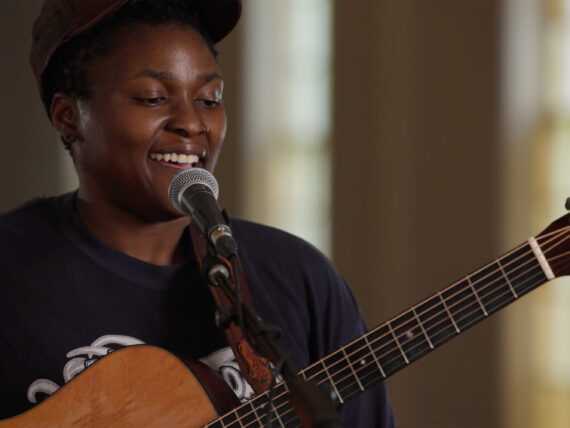 A woman holding a guitar at a microphone