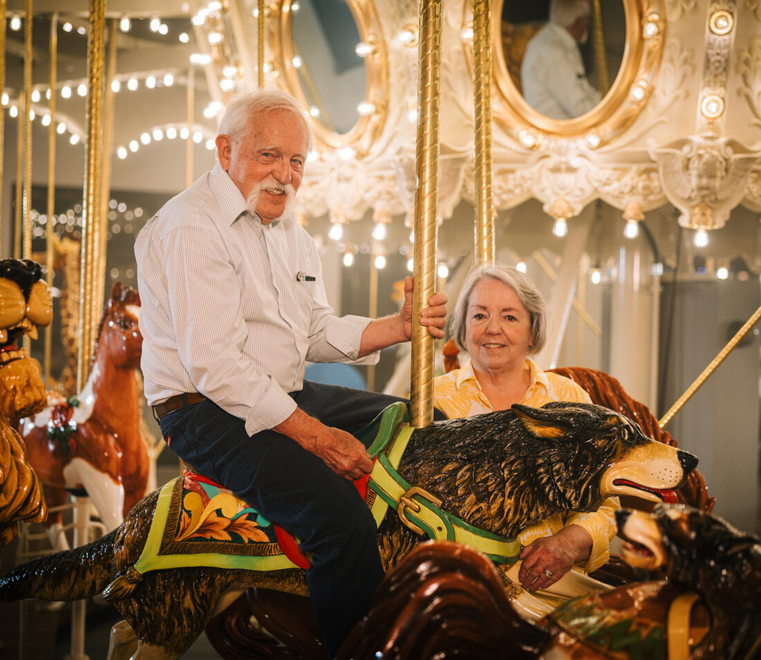 An older couple smiles on a carousel