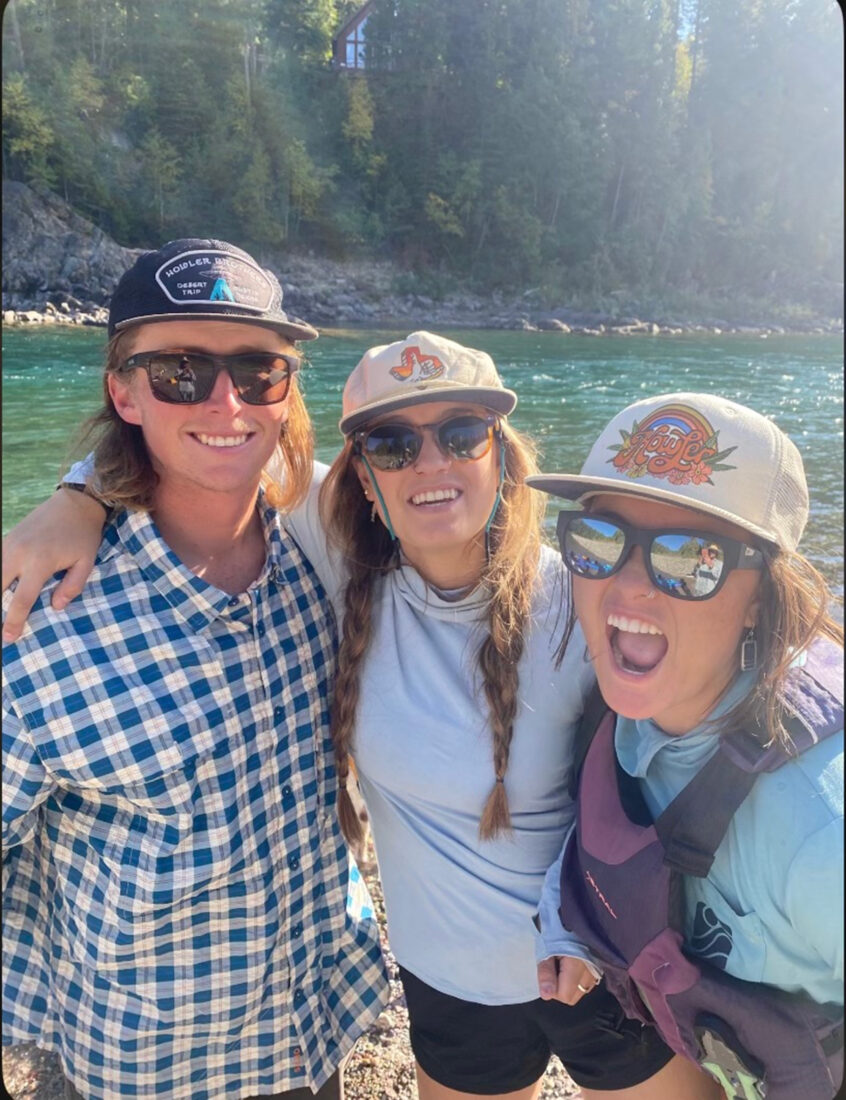 A brother and two sisters pose on the bank of a river