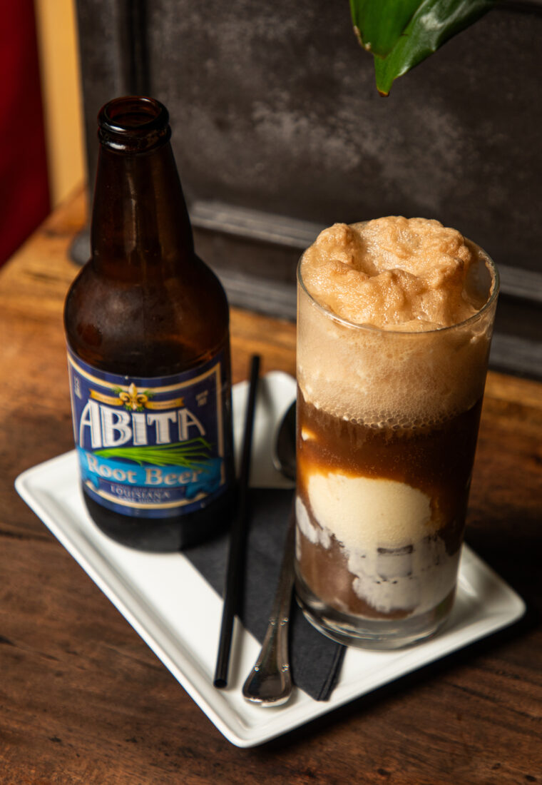 A tall glass of a root beer float with a bottle of root beer