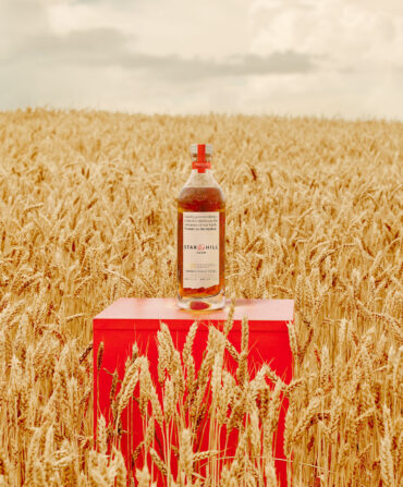 A bottle of whiskey in a wheat field on a red stand