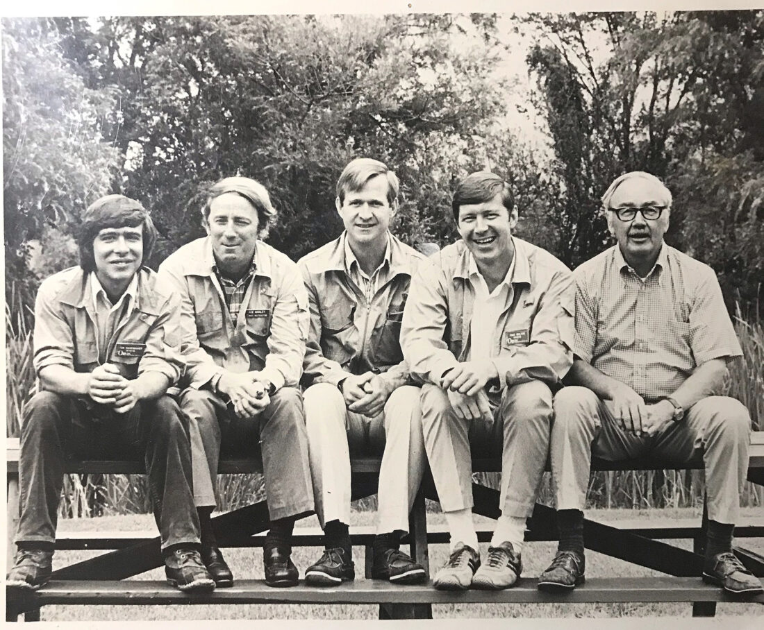 Five men pose while sitting in a row