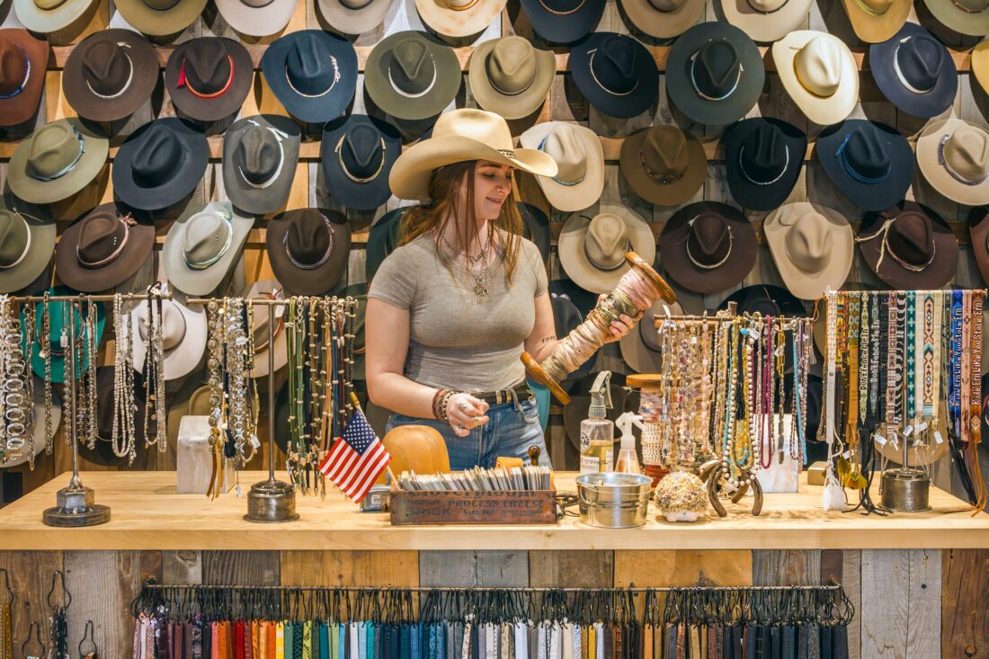A woman stands behind a counter with rows of western hats
