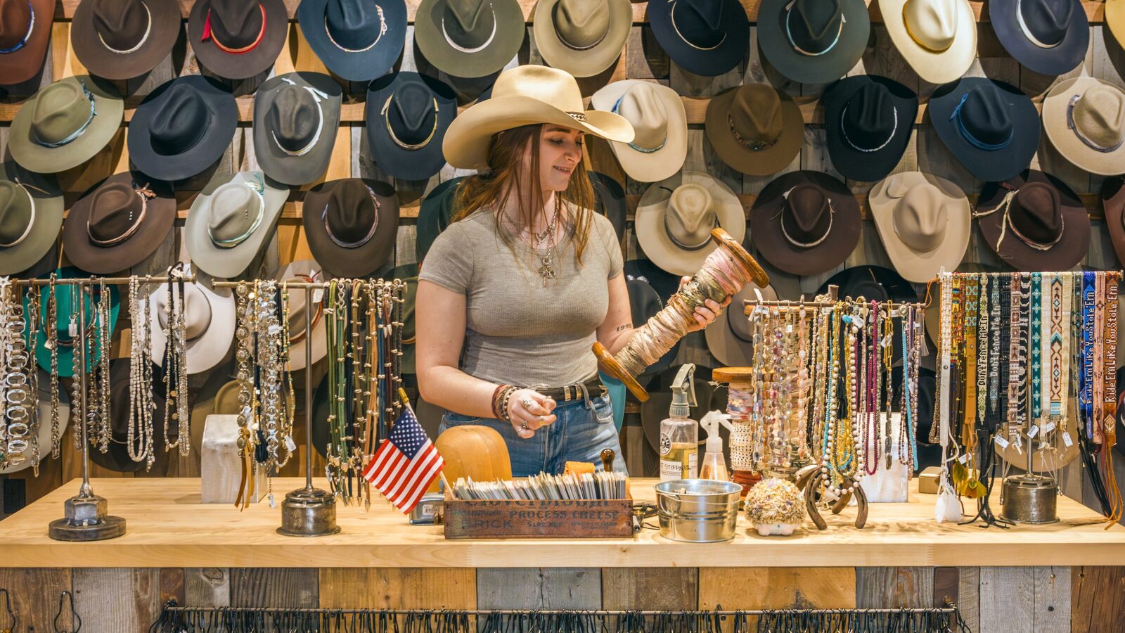 A woman stands behind a counter with rows of western hats