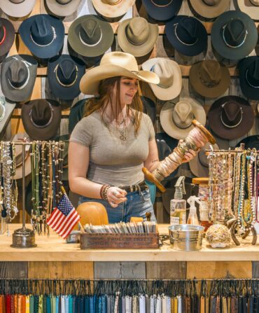 A woman stands behind a counter with rows of western hats