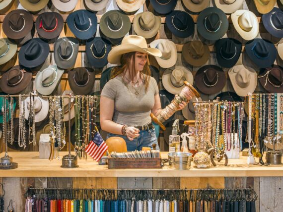 A woman stands behind a counter with rows of western hats