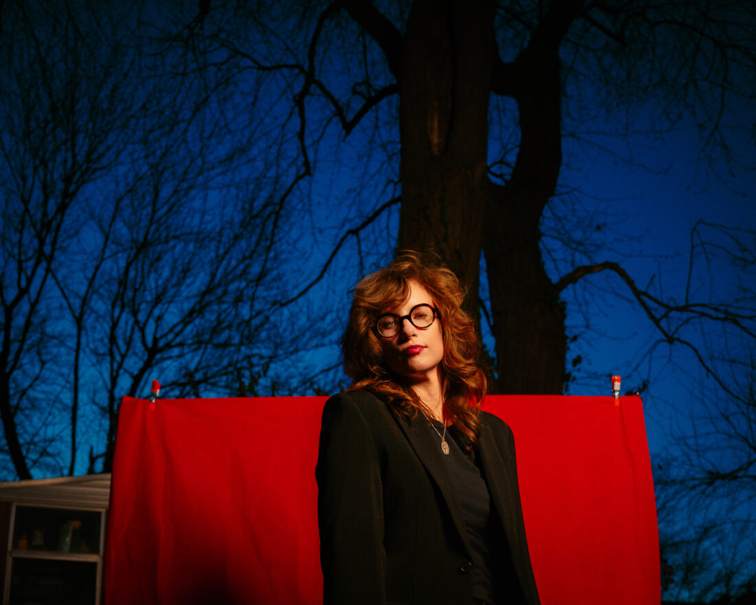 A woman with glasses stands outside in front of a red drop cloth