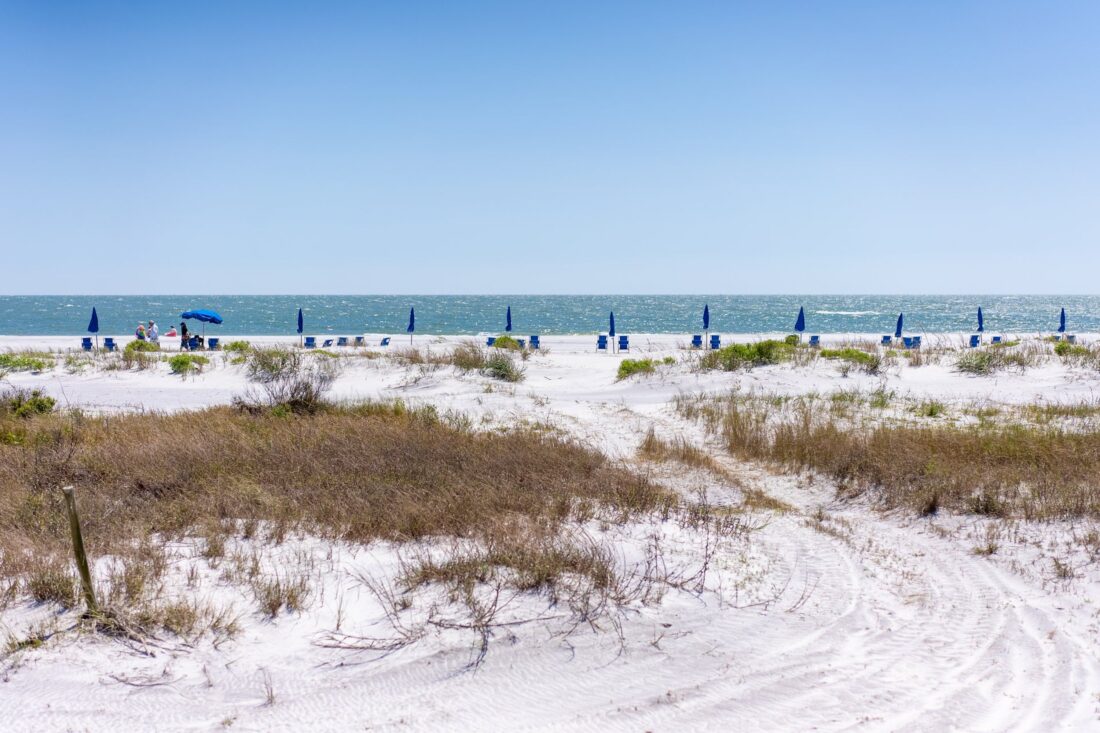 Blue umbrellas and chairs dot a white beach
